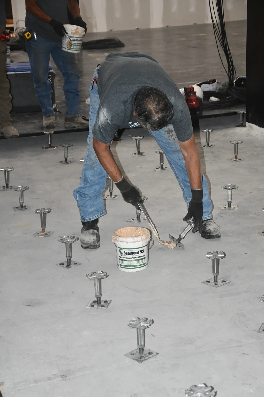 Installer applying adhesive at a raised floor pedestal base at Coyote Valley Casino